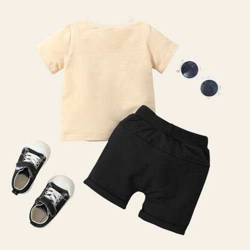 Children's outfit with yellow shirt, black shorts, and shoes on a light wooden surface.
