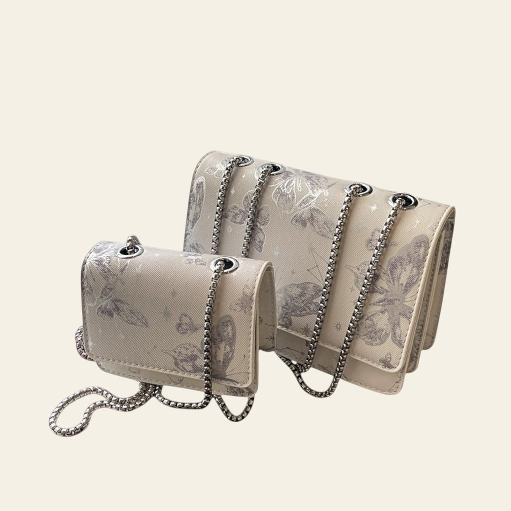 White handbag with butterfly design and chain strap on a windowsill.