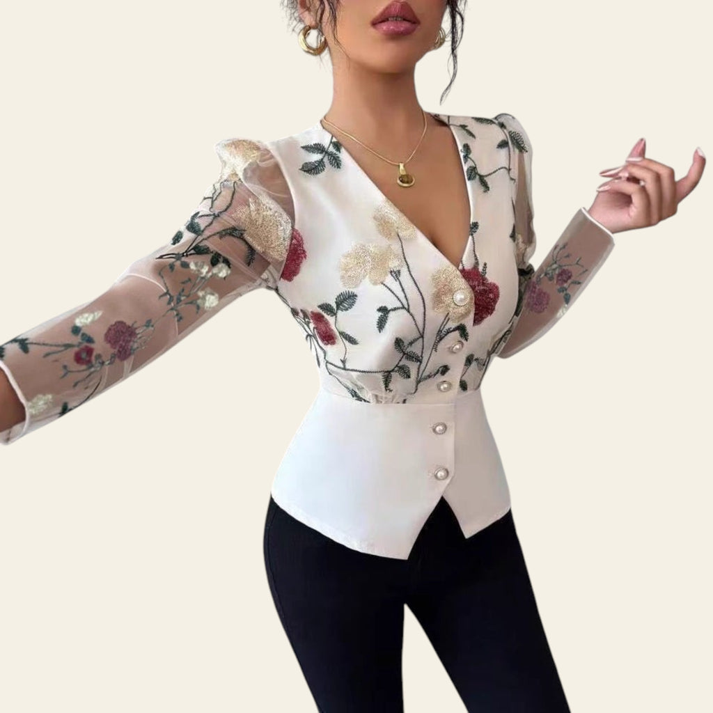 Woman wearing a floral blouse with long sleeves and black pants in a room.