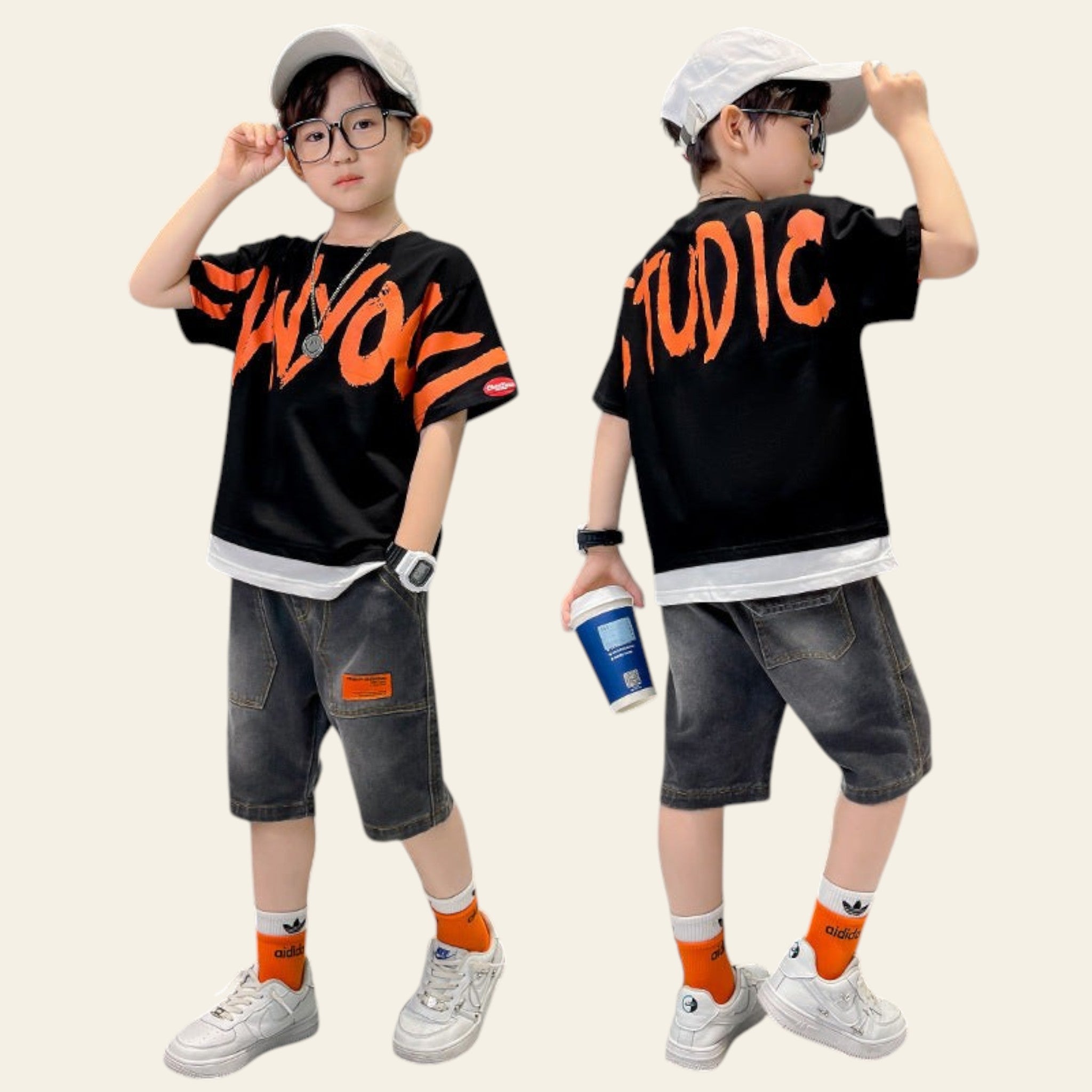 Child wearing a black t-shirt with orange text, gray shorts, and white sneakers, holding a cup.