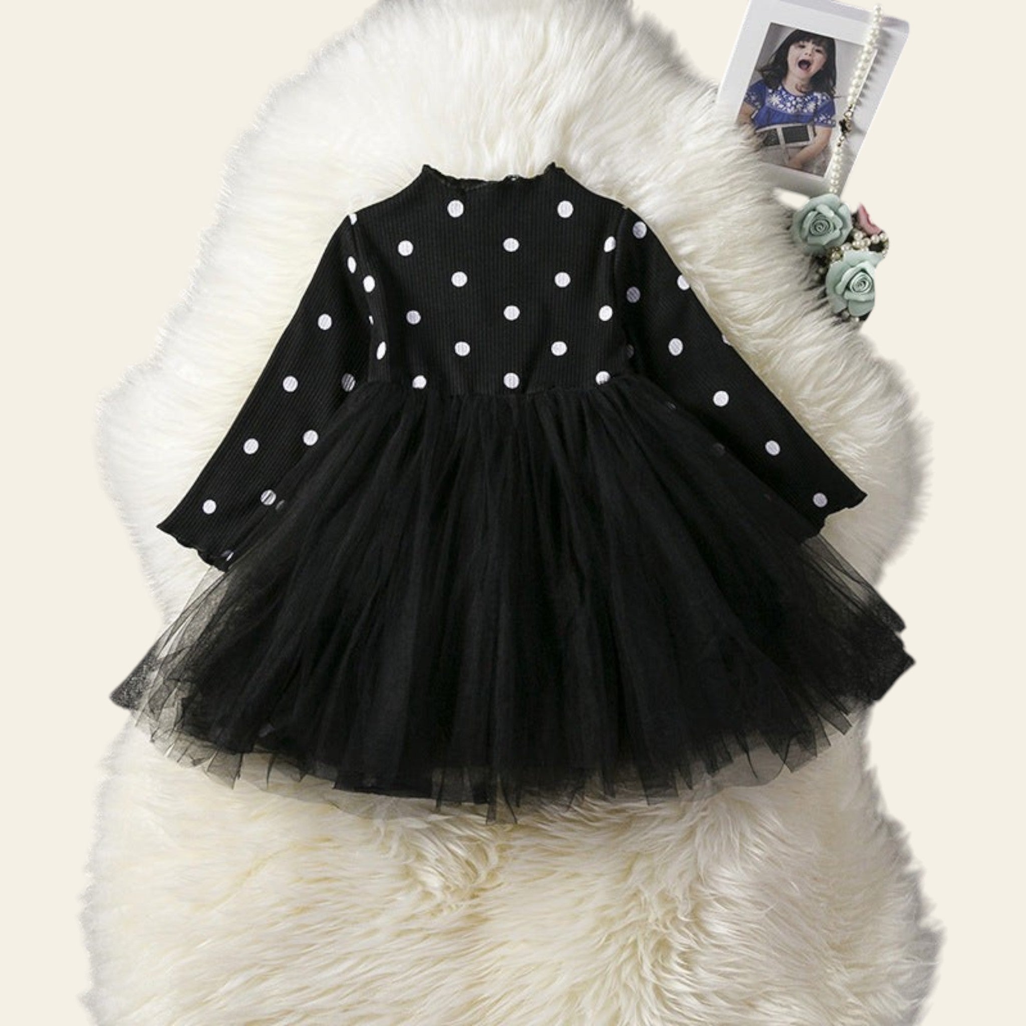 Black polka dot dress with a tulle skirt on a white fur surface.