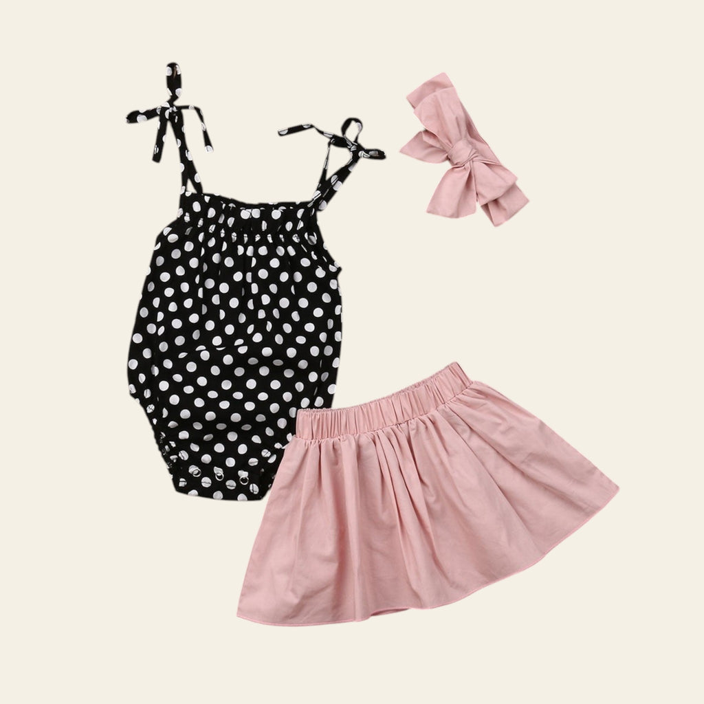 Black polka dot romper with pink skirt and headband on a wooden surface