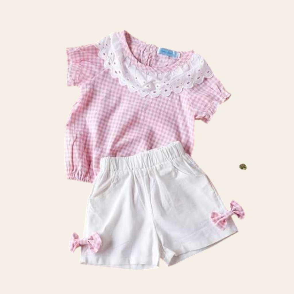 Pink checkered top and white shorts with pink bows on a wooden surface.