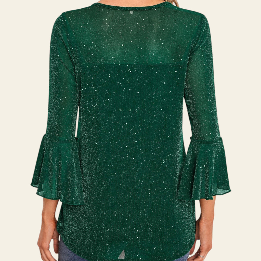 Green blouse with ruffled sleeves worn by a person, against a decorative wall.