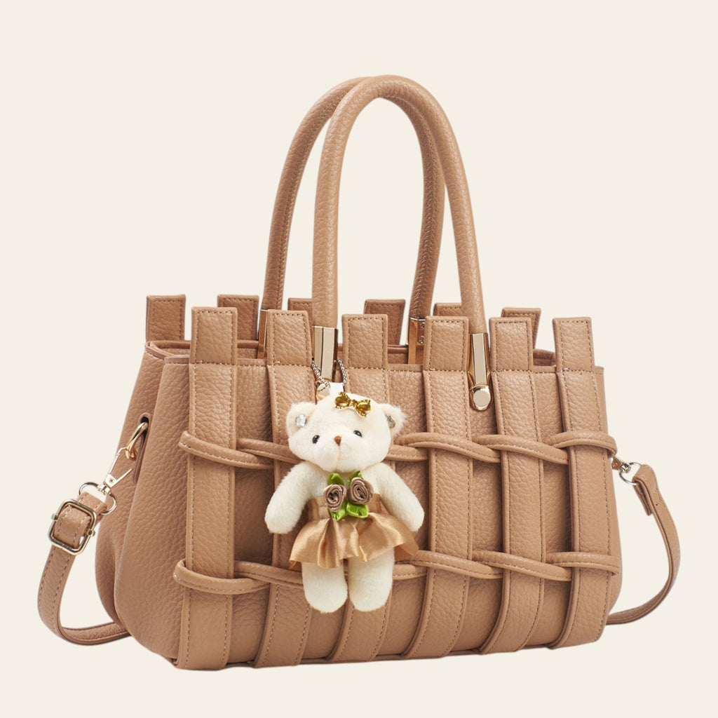 Beige handbag with a teddy bear charm on a white background