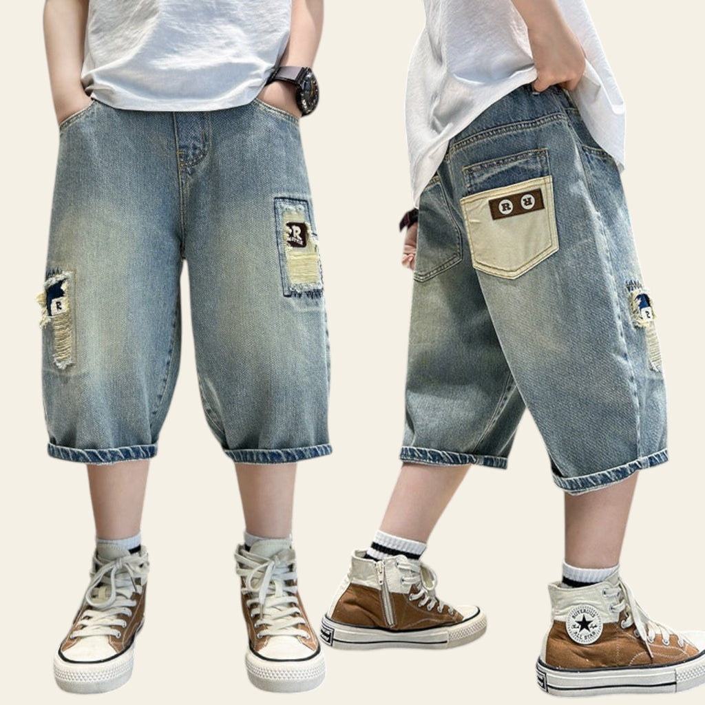 Denim shorts with patches and a person wearing them with brown sneakers on a metallic surface.