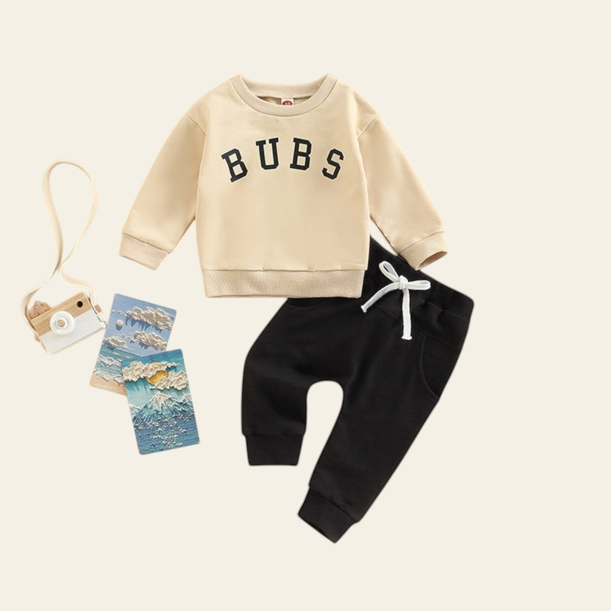 Children's beige sweatshirt with 'BUBS' text and black pants on a beige background