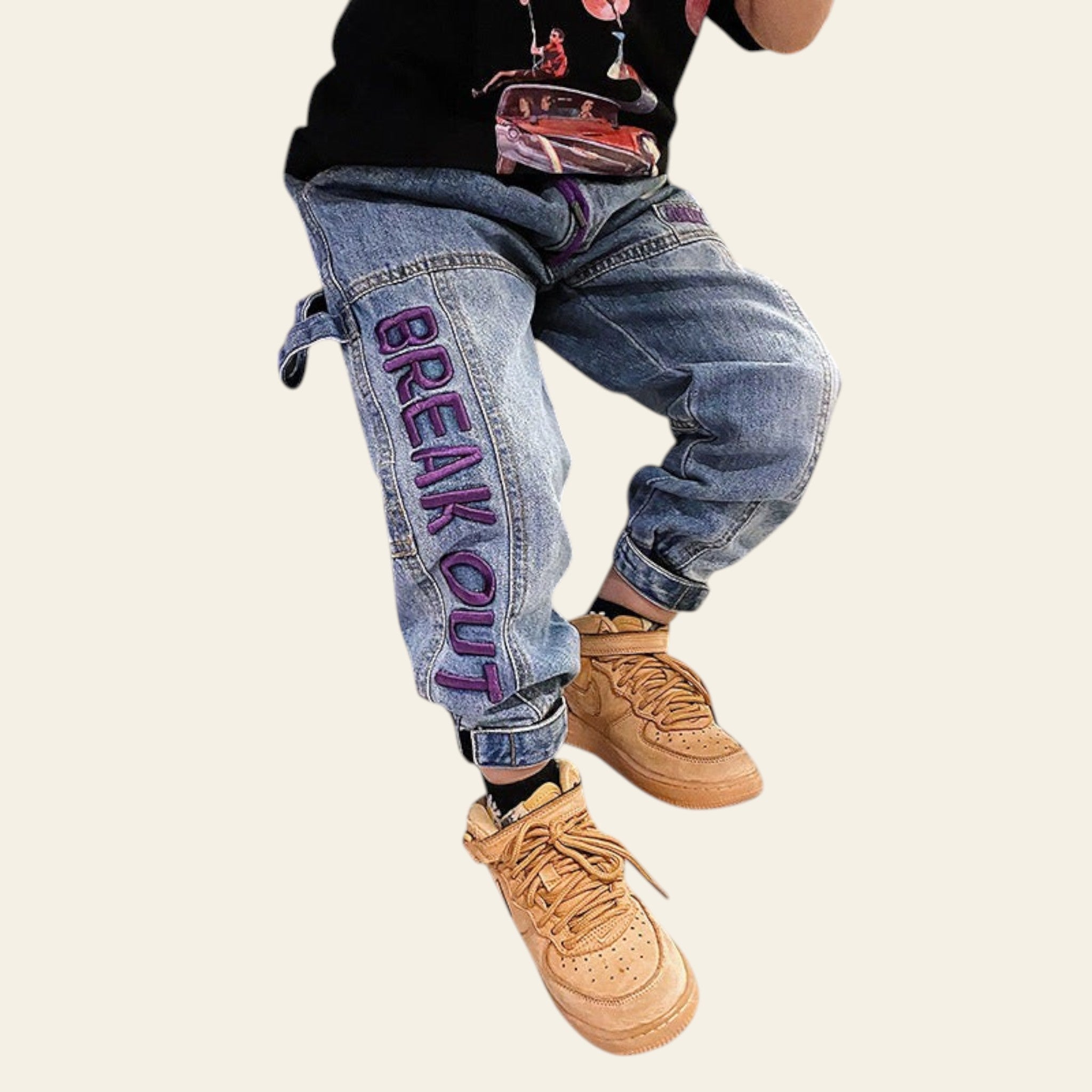Person wearing blue jeans with 'BREAK OUT' text and tan boots in a casual setting.