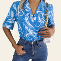 Person wearing a blue and white patterned shirt and blue jeans, holding a gold handbag.
