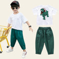 Child wearing a white t-shirt with a dinosaur graphic and green pants on a street.
