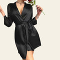 Person wearing a black satin robe holding a red rose against a neutral background