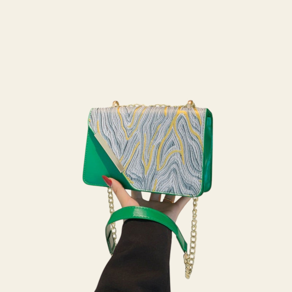 Green handbag with gold chain held by a hand against a black background