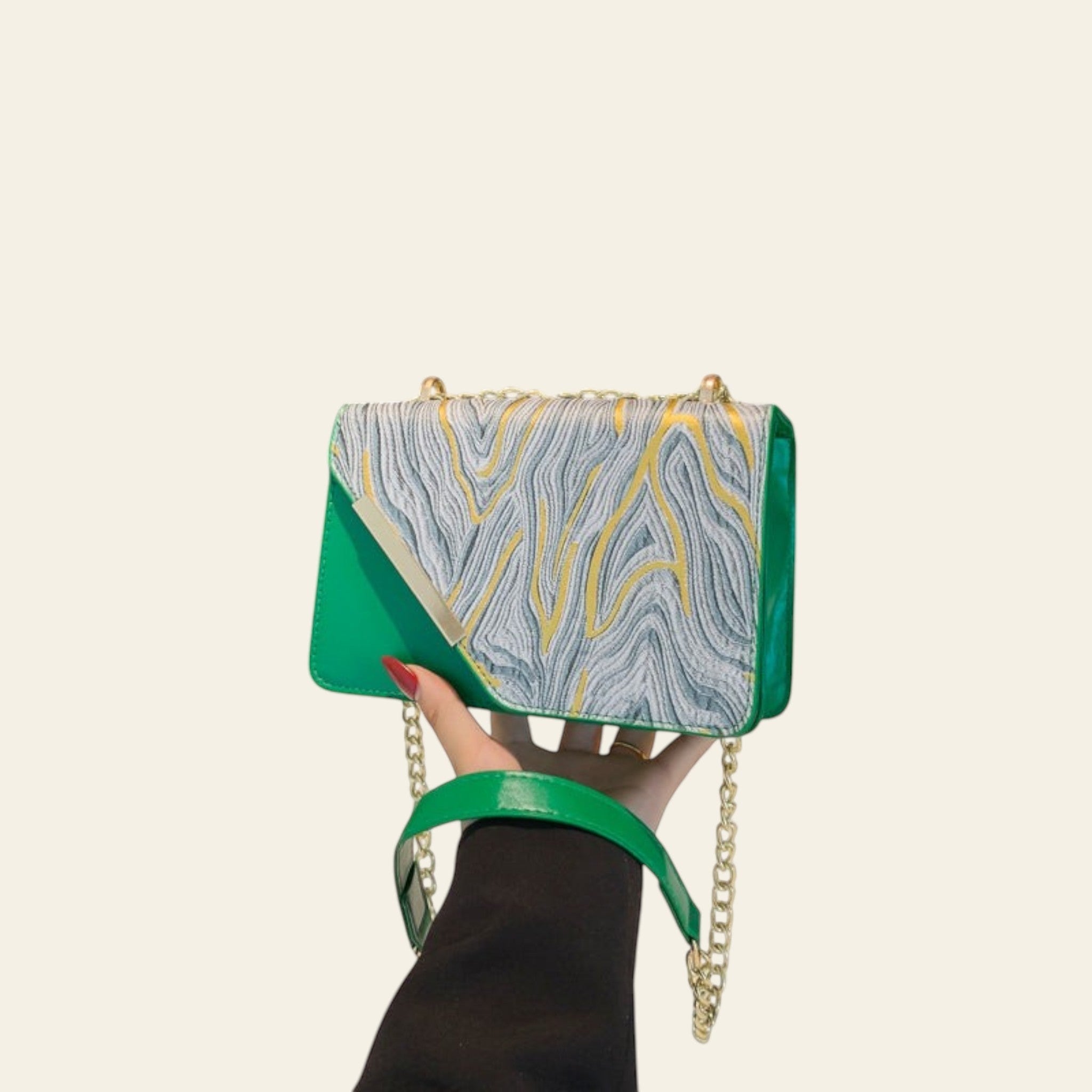 Green handbag with gold chain held by a hand against a black background