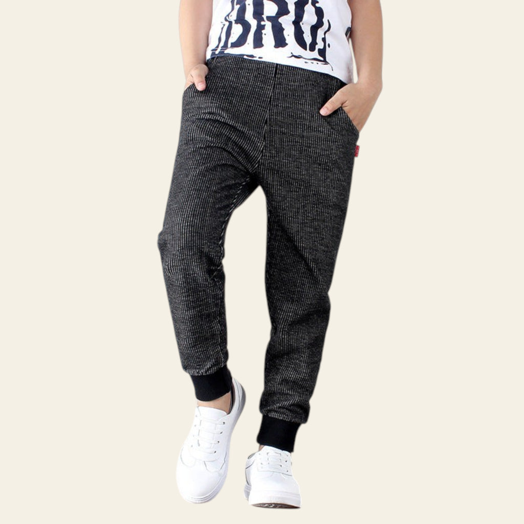 Person wearing black checkered jogger pants with white sneakers on a light wooden floor.