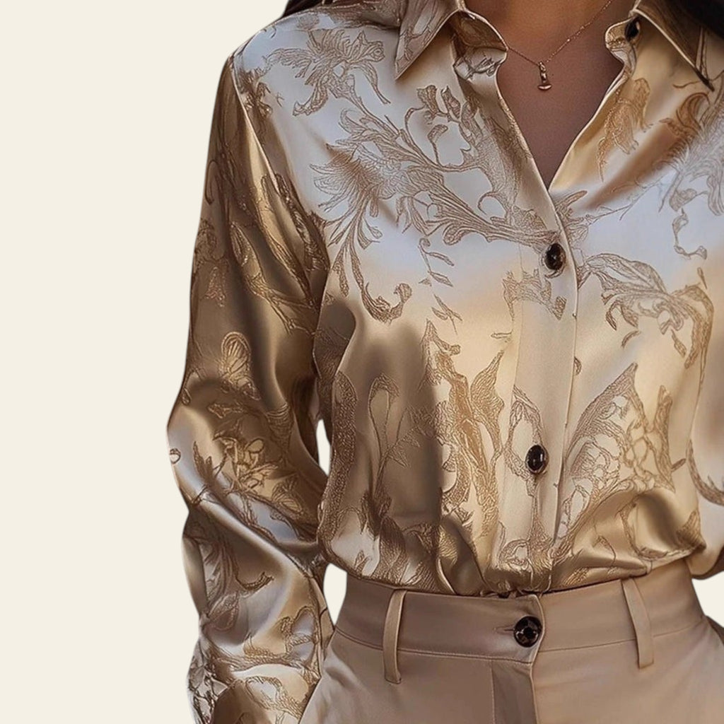 Beige patterned blouse with black buttons worn by a person, blurred background