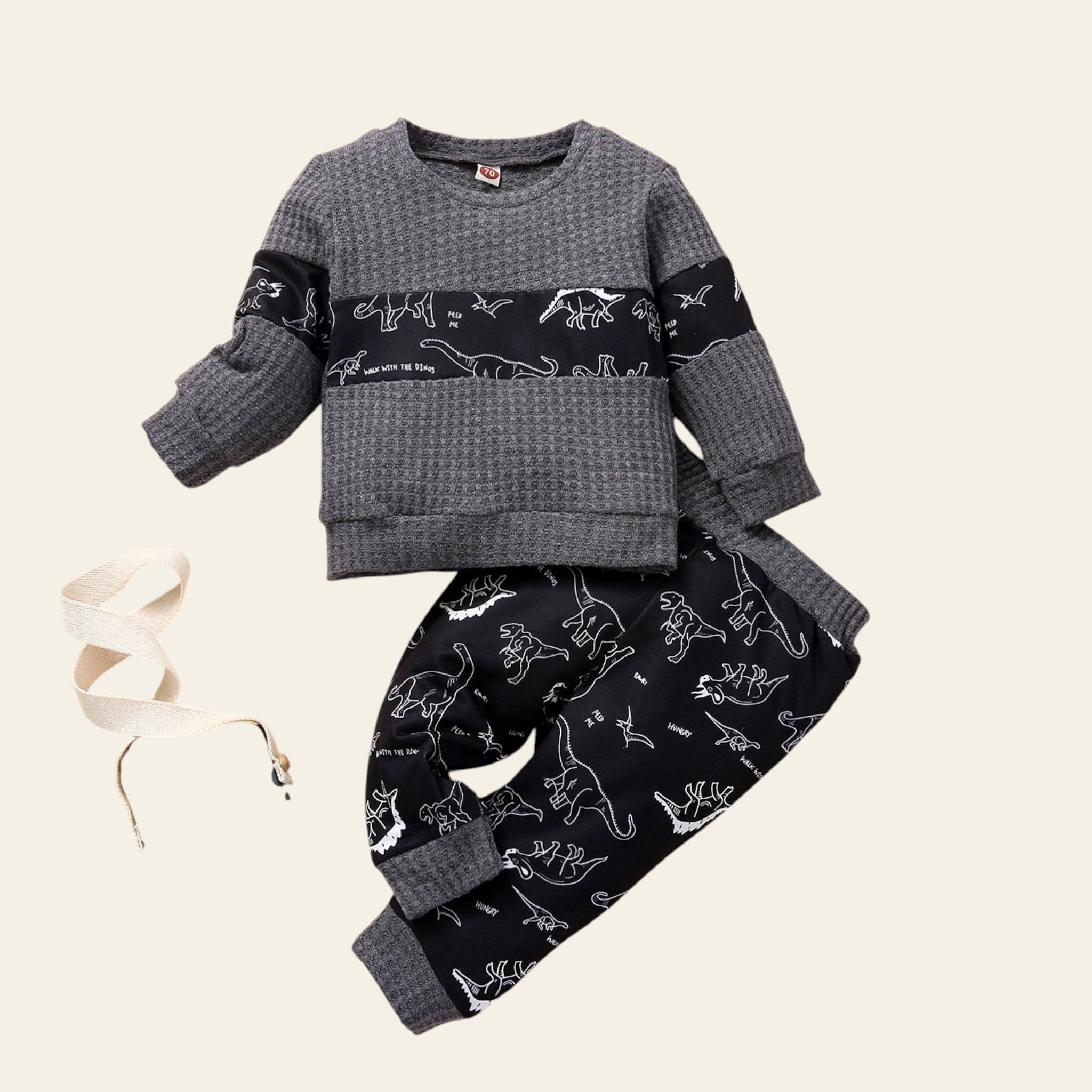 Children's outfit with gray top and black pants featuring dinosaur prints on a wooden surface.