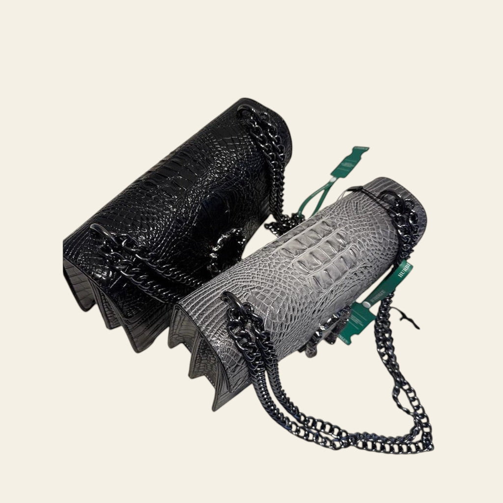 Two handbags, one black and one gray with chain detail, on a white surface.