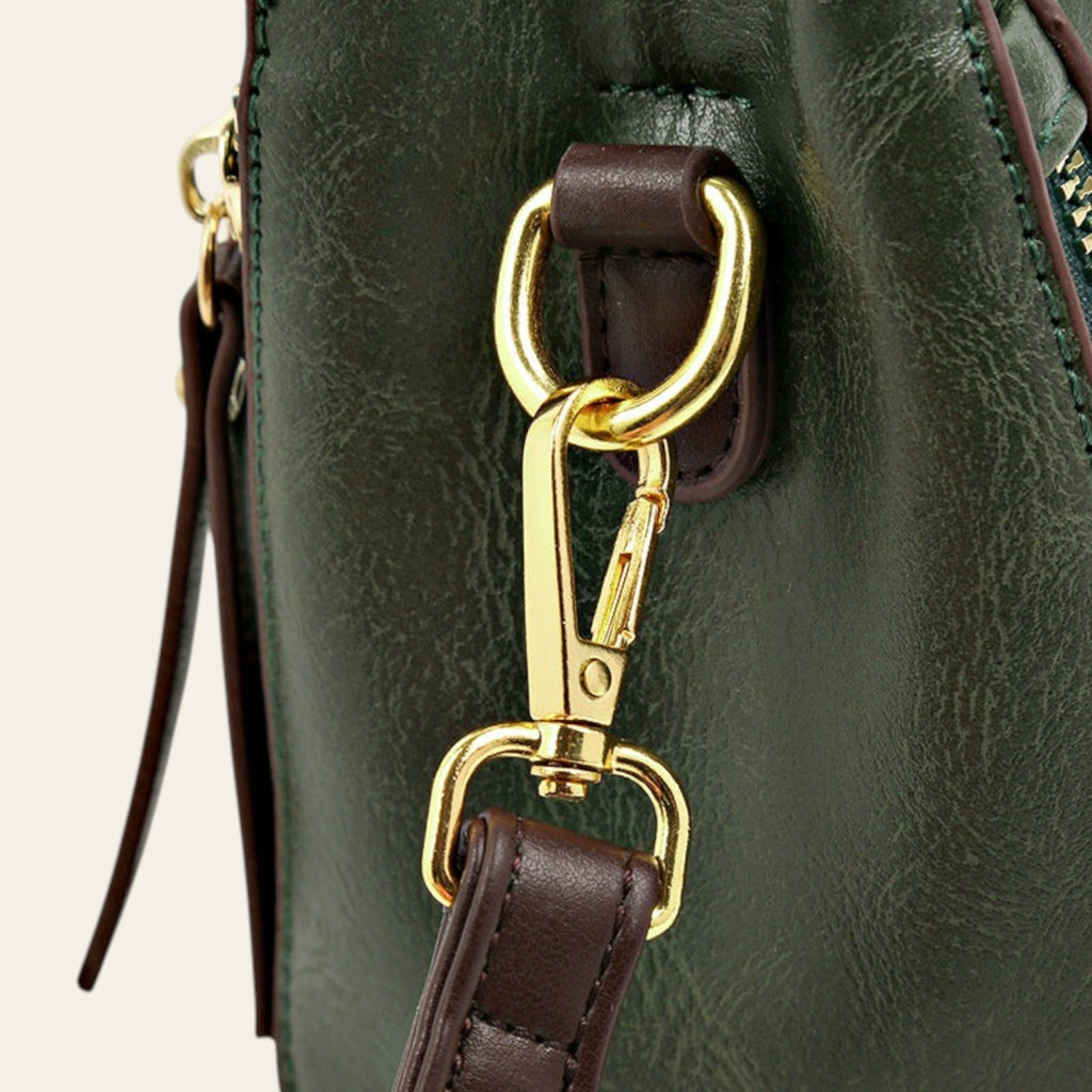 Close-up of a green leather bag with gold clasp and brown strap.