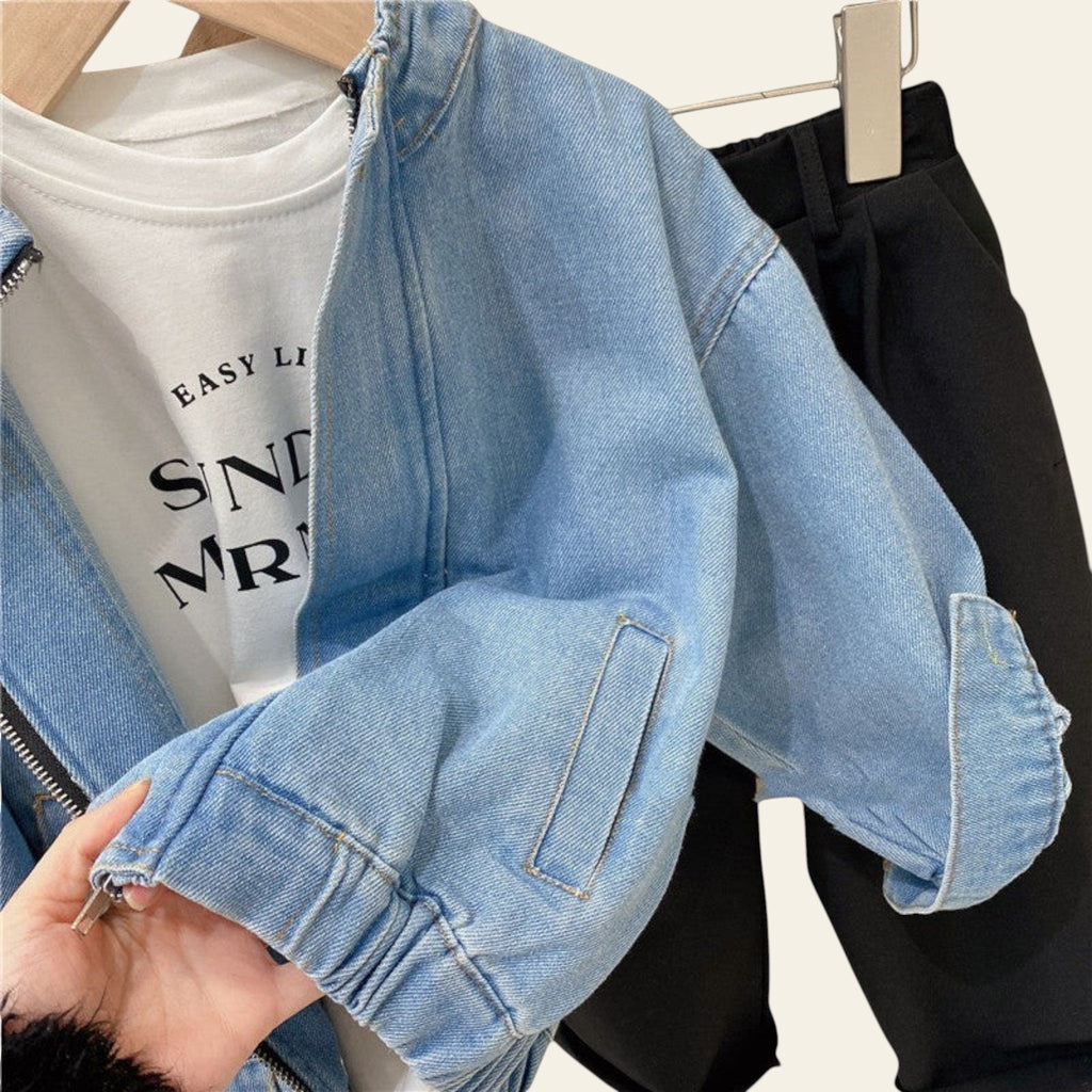 Light blue denim jacket held by a hand with a white t-shirt and black pants in the background.