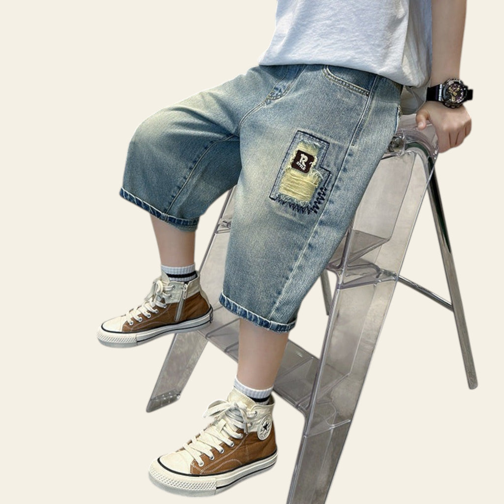 Person wearing denim shorts and brown sneakers sitting on a transparent stool.