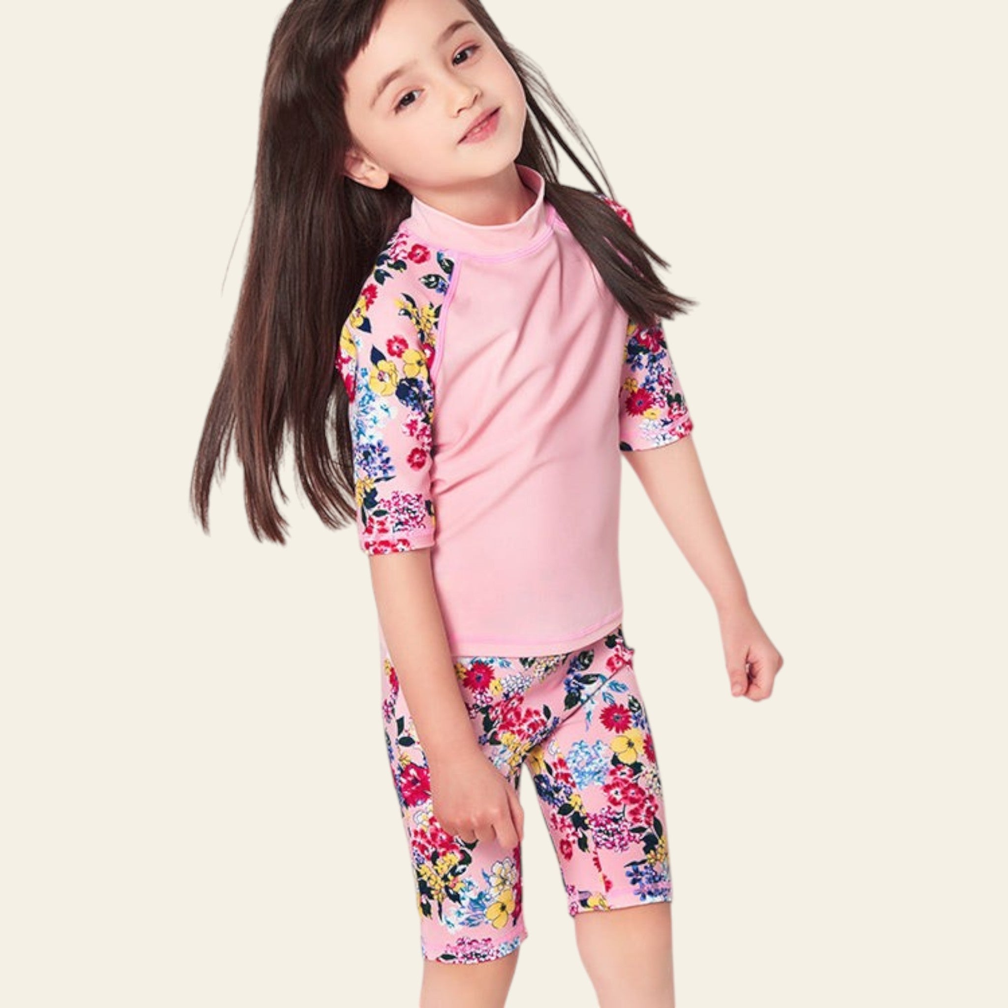 Young girl wearing a pink floral rash guard and shorts on a light gray background