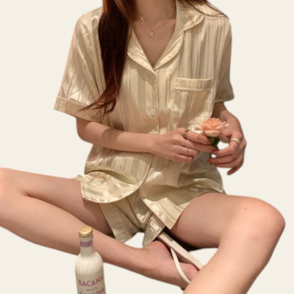 Person wearing a light-colored satin outfit holding a bottle and a glass.