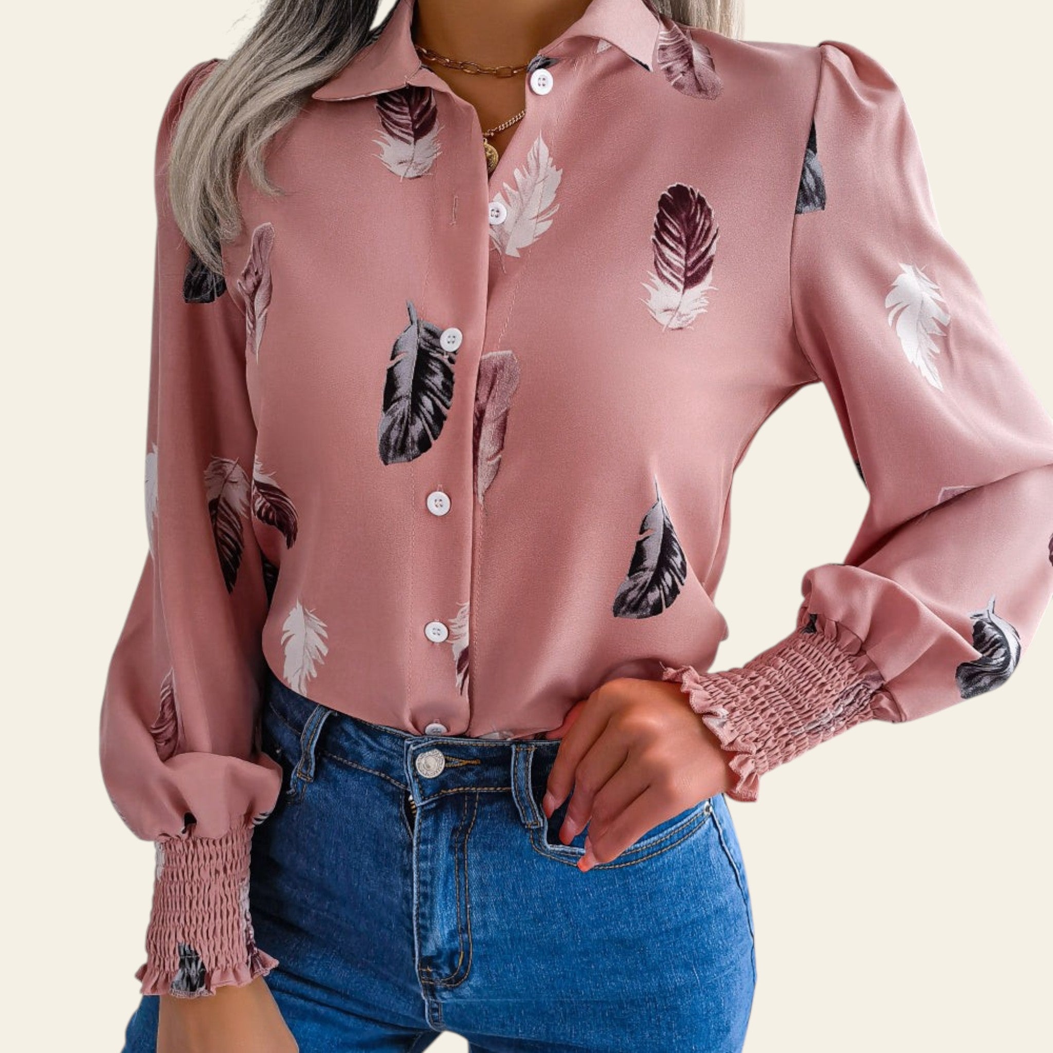 Person wearing a pink blouse with feather pattern and blue jeans on a neutral background