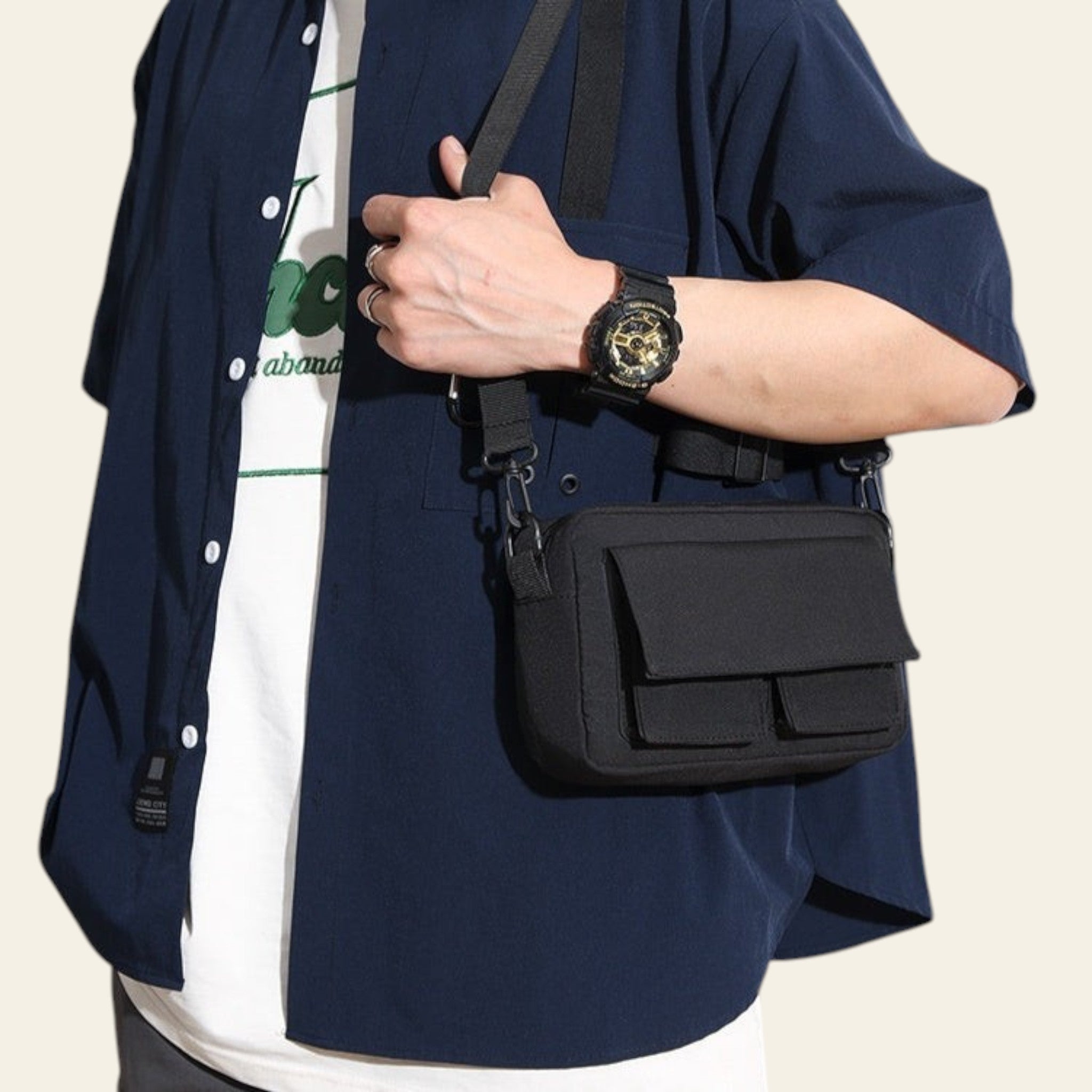 Person wearing a navy blue shirt with a black crossbody bag and a watch on a blurred background