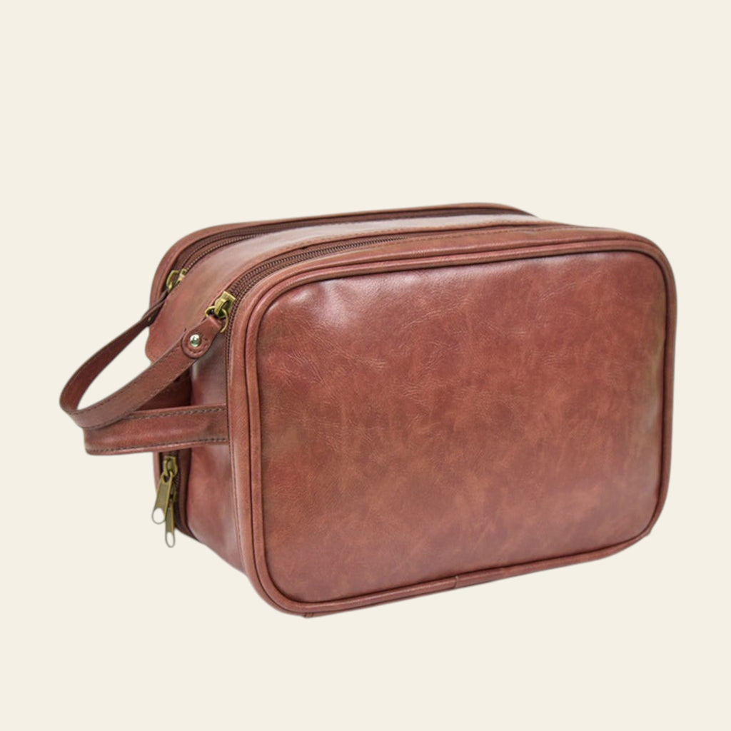 Brown leather toiletry bag with zippers on a white background