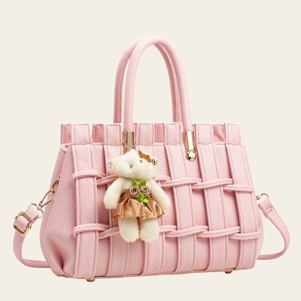 Pink textured handbag with a teddy bear charm on a light gray background