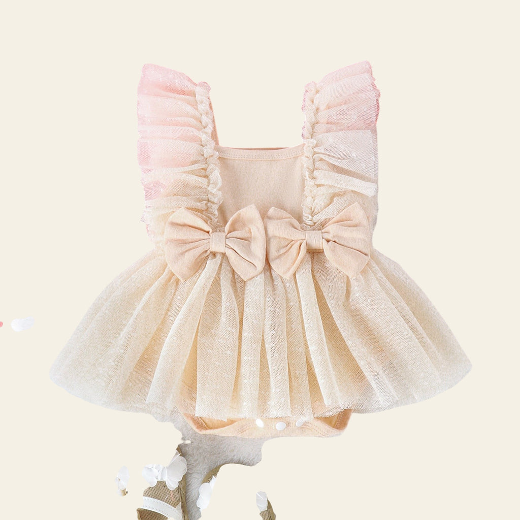 Beige baby dress with ruffles and bows on a pink and white background with toys and flowers.