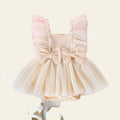 Beige baby dress with ruffles and bows on a pink and white background with toys and flowers.