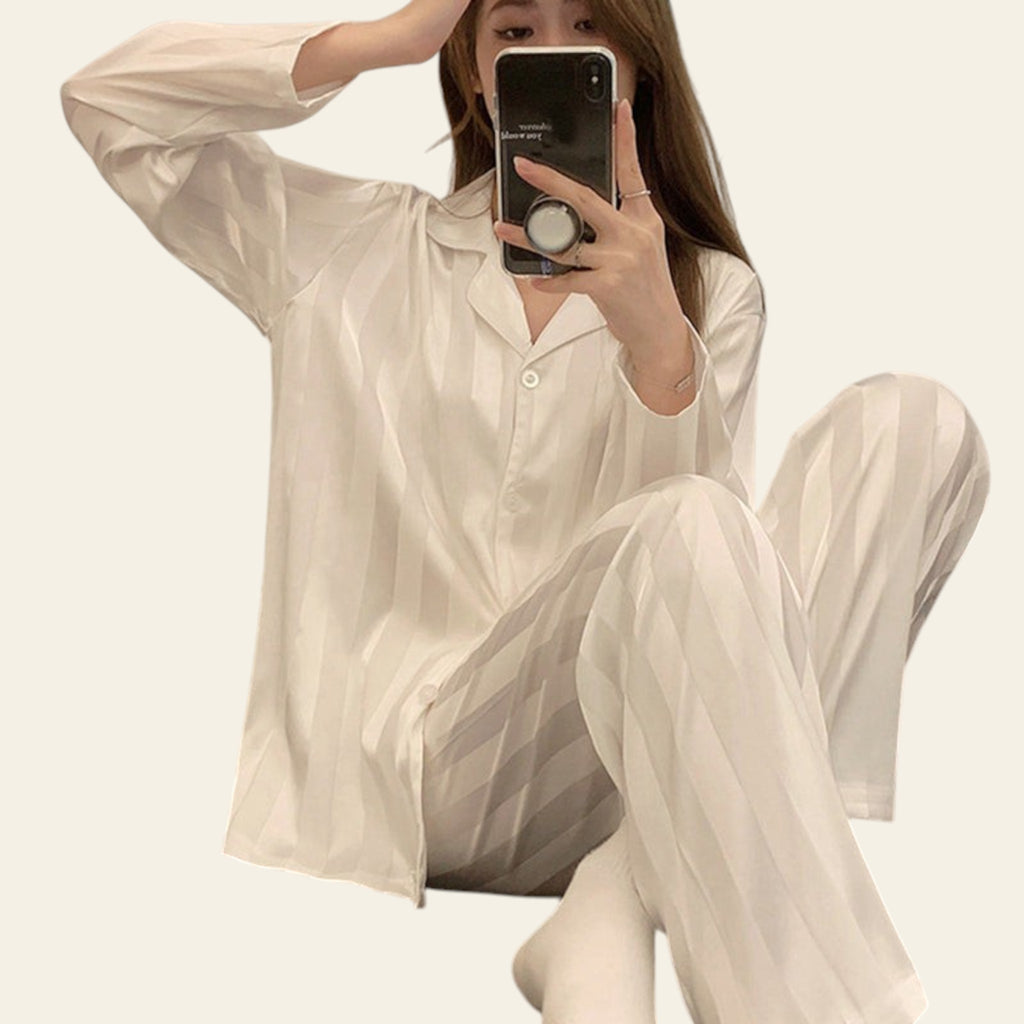 Person wearing a white satin pajama set sitting on a bed.