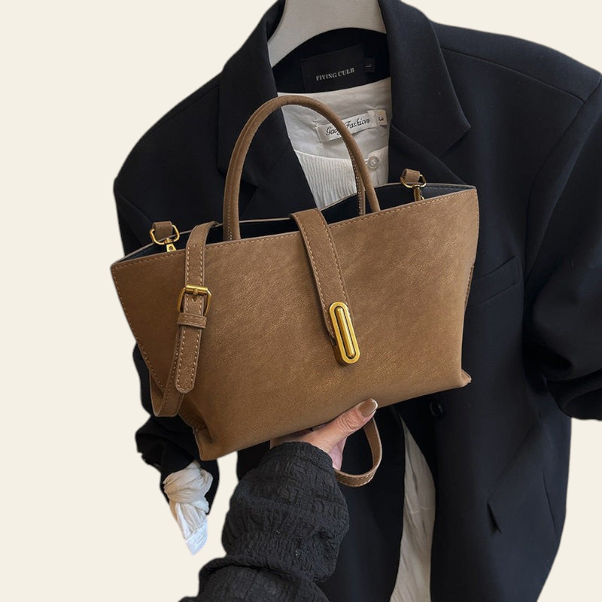 Brown handbag held by a person wearing a black coat and white shirt.