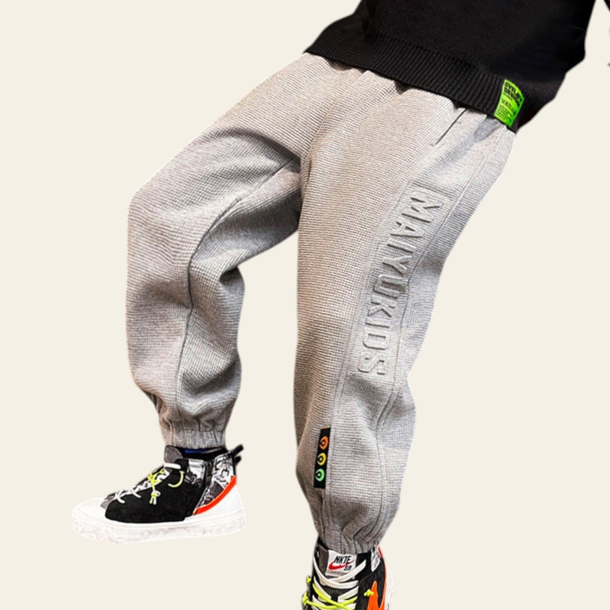 Person wearing gray jogger pants with branding, standing on a wooden floor.