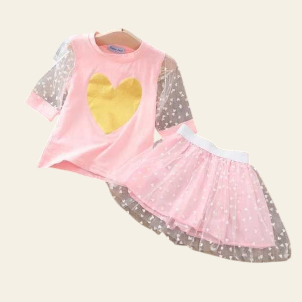 Children's outfit with pink top and skirt featuring a yellow heart on a wooden surface.