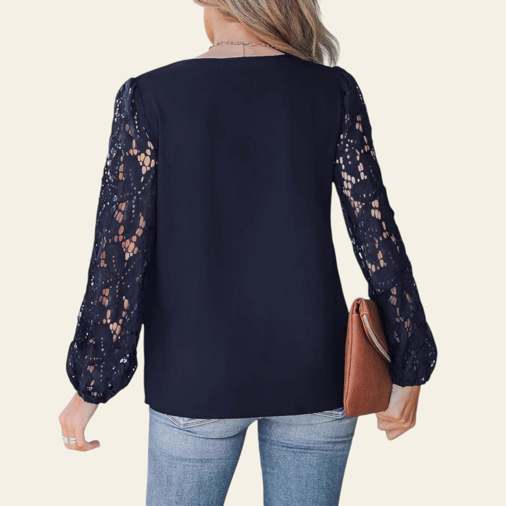 Woman wearing a navy blue blouse with lace sleeves and holding a brown clutch.