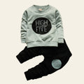 Children's outfit with light blue sweatshirt and black pants on a wooden surface with decorative elements.