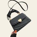 Black quilted handbag with a heart-shaped clasp held by a hand on a light background