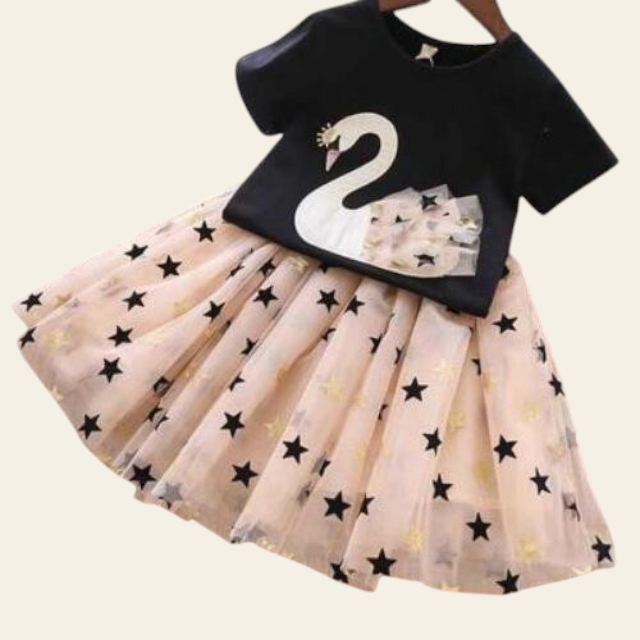 Black top with a white swan design and beige skirt with star patterns on a wooden surface.