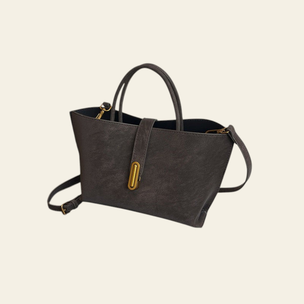 Gray handbag with gold accents on a black leather chair against a white wall.