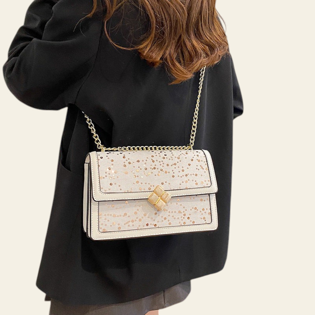 Person wearing a black coat with a white handbag featuring gold accents.