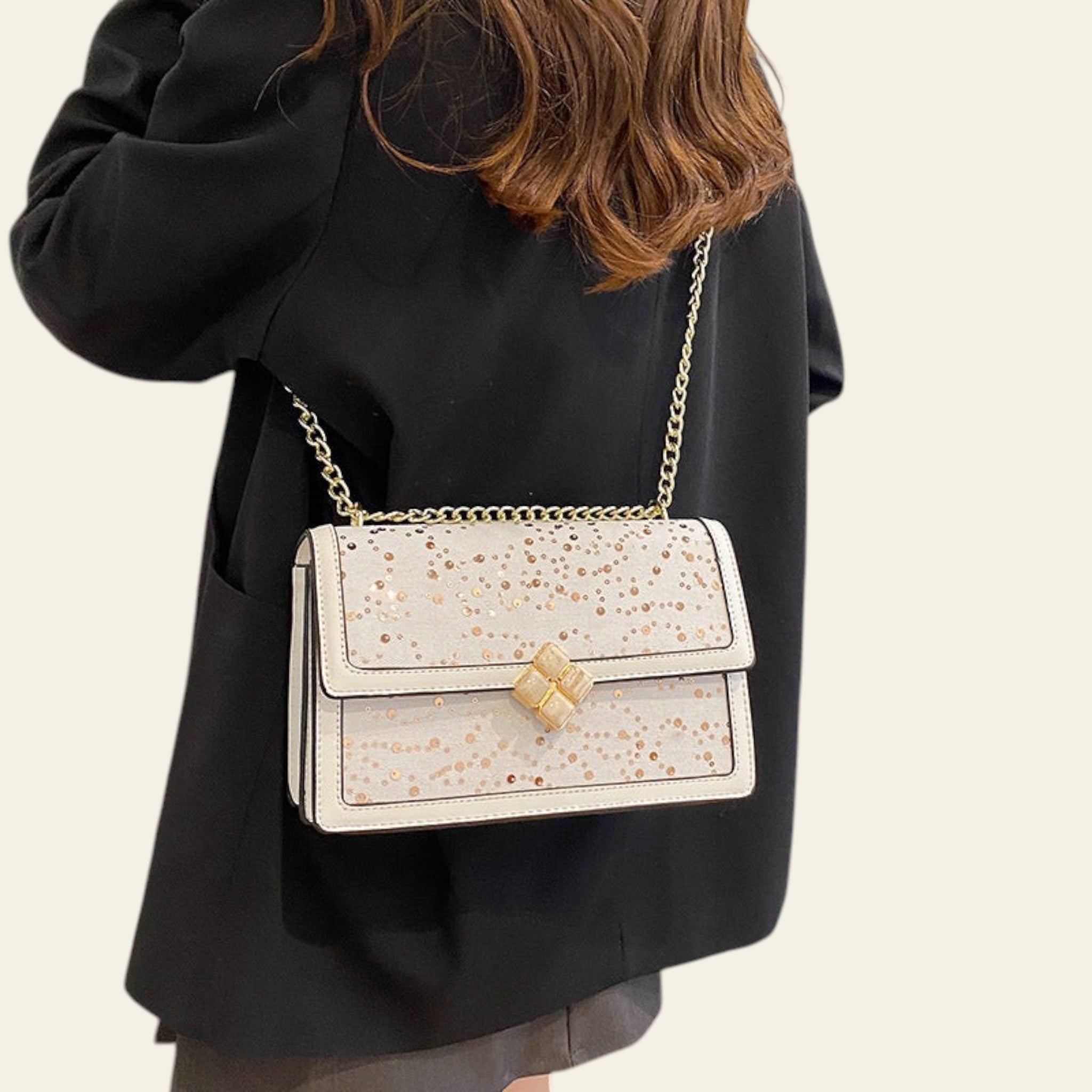 Person wearing a black coat with a white handbag featuring gold accents.