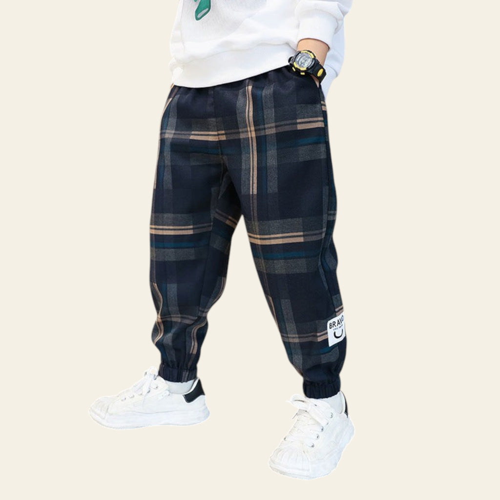 Person wearing navy plaid pants with a white label, white sneakers, and a white sweatshirt in a cafe setting.