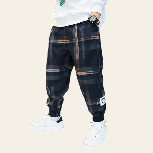 Person wearing navy plaid pants with a white label, white sneakers, and a white sweatshirt in a cafe setting.
