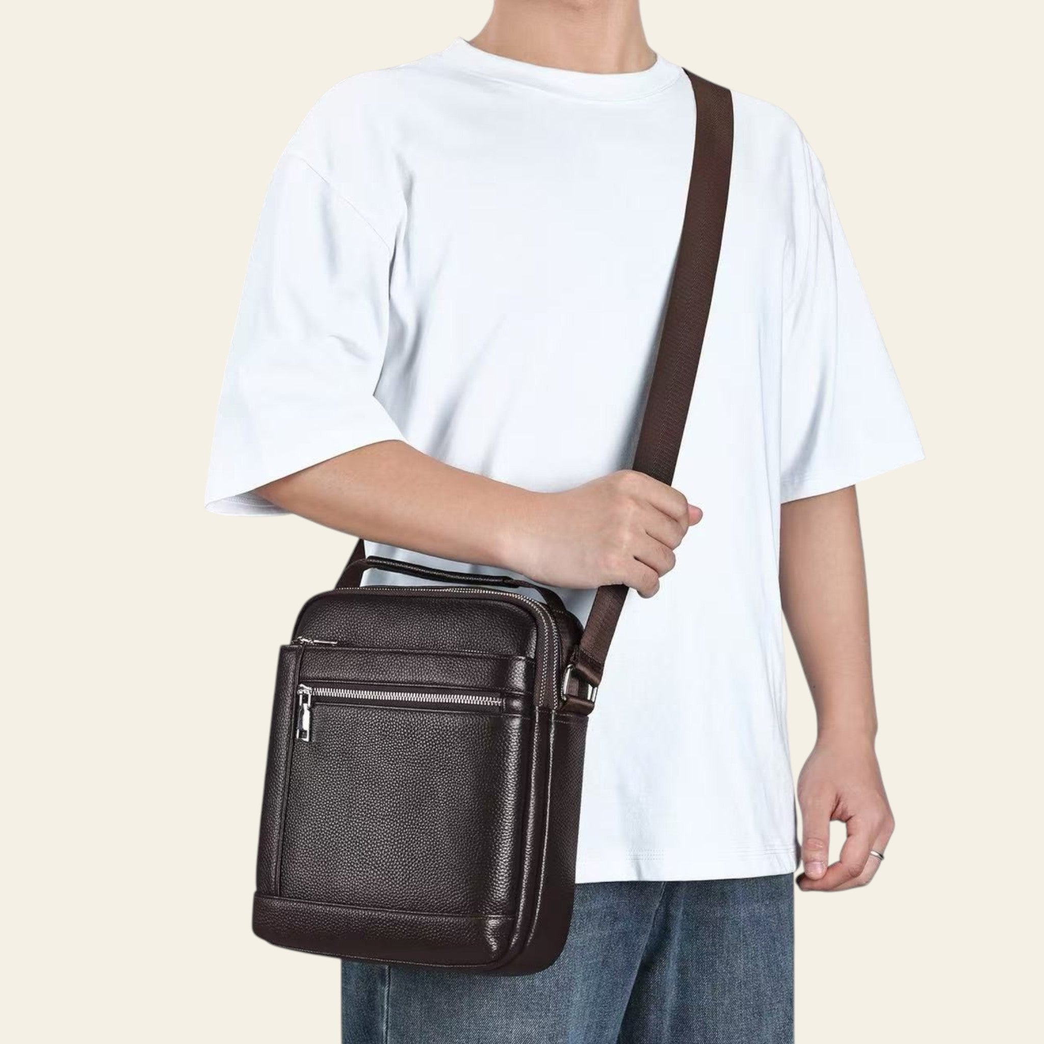 Person wearing a brown leather crossbody bag on a plain background