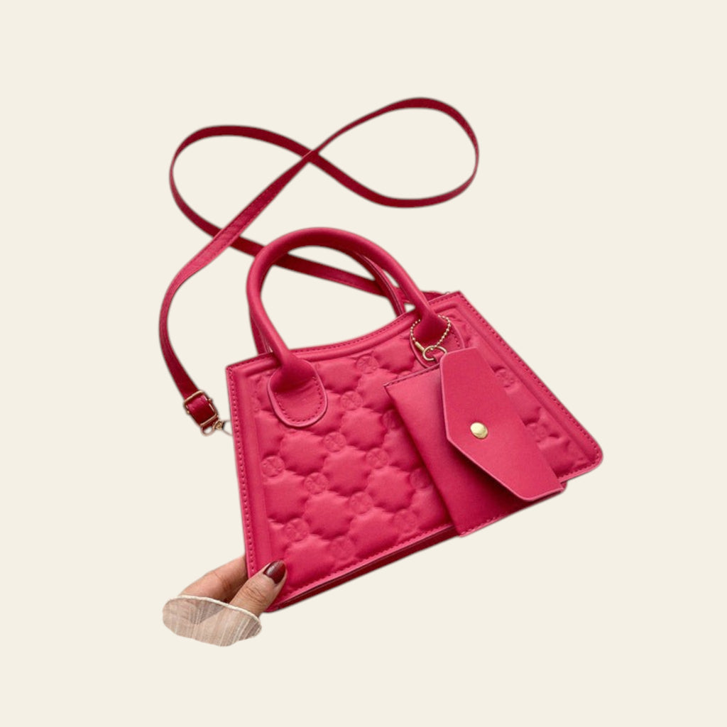Pink quilted handbag with matching strap held against a light background