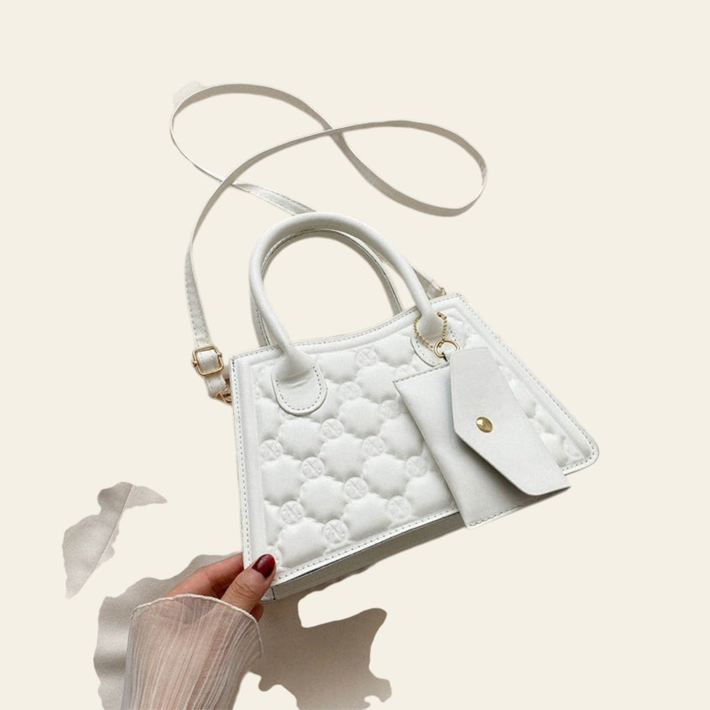 White quilted handbag held by a hand with red nail polish, on a light beige background.
