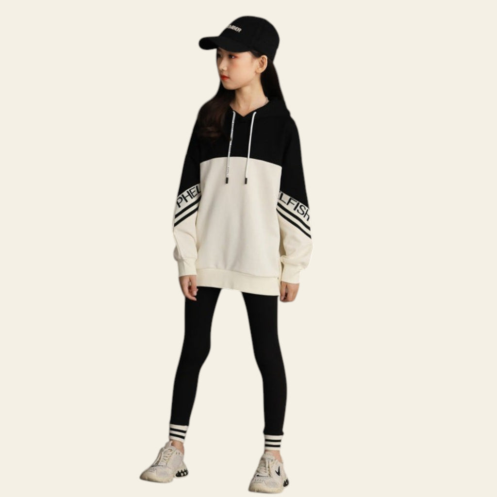 Person wearing a black and white hoodie with striped pants against a concrete wall.