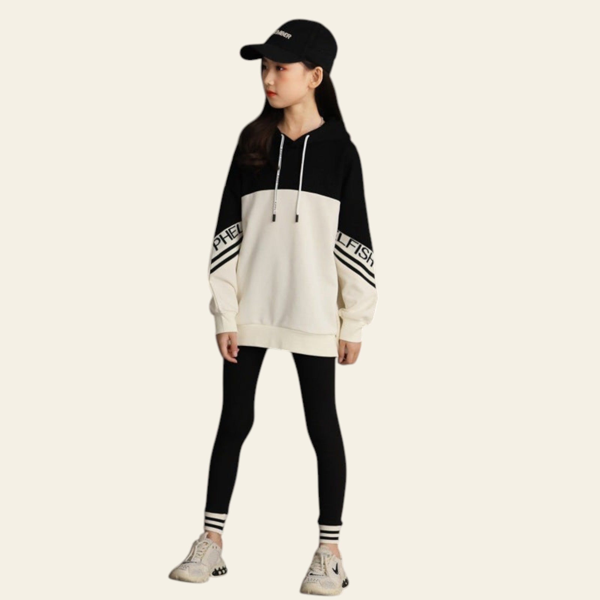Person wearing a black and white hoodie with striped pants against a concrete wall.